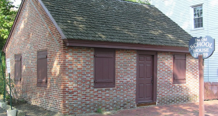 Image Of A Single Story, Small Brick Building With A Dark Brown Door And Closed Window Shutters.